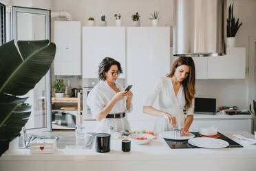 Two smiling women with brown hair standing in a kitchen, preparing food. - CUF56537