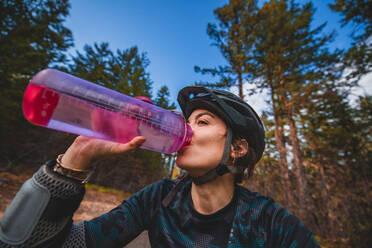 Mountainbikerin trinkt aus einer Wasserflasche im Wald - CUF56554