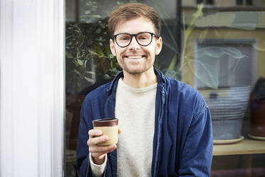 Portrait of smiling man having coffee outside art studio - MASF19533