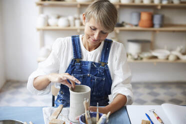 Mature woman molding earthenware at table in art class - MASF19574