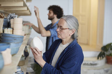 Man and woman arranging earthenware on shelf in art class - MASF19599