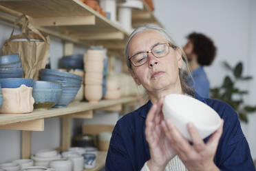 Mature woman examining bowl in art class - MASF19600