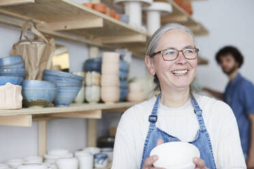 Smiling mature woman looking away while holding bowl in pottery class - MASF19602