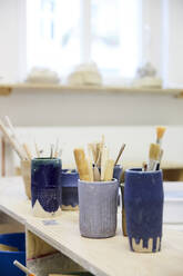 Various paintbrushes in containers on table at workshop - MASF19620