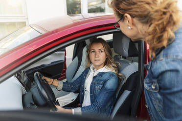 Daughter looking at mother while learning car to drive during vacations - MASF19685