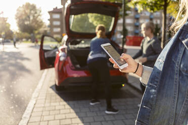 Midsection of teenager texting while mother and son standing near car trunk - MASF19686