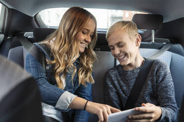 Smiling siblings using phone while sitting in car - MASF19687