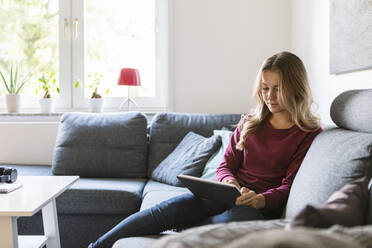 Weiblicher Teenager, der ein digitales Tablet benutzt, während er zu Hause auf dem Sofa sitzt - MASF19708