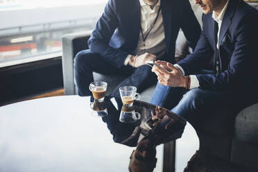 Businessman showing laptop to colleague while sitting on sofa at workplace - MASF19742