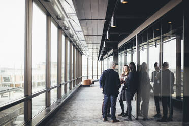 Smiling female entrepreneur talking to colleagues in office corridor - MASF19745