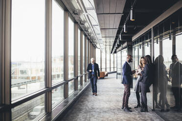 Smiling entrepreneurs talking while colleague walking in office corridor - MASF19747