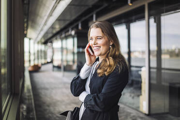 Lächelnde Geschäftsfrau, die am Telefon spricht, während sie am Arbeitsplatz steht - MASF19756