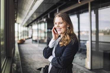 Smiling businesswoman talking on phone while standing at workplace - MASF19756