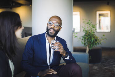 Businessman with drinking glass looking at coworker in office - MASF19816