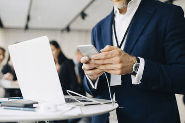 Midsection of male entrepreneur using phone while standing in office seminar - MASF19867