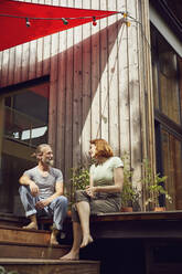 Paar im Gespräch, während es vor einem kleinen Haus sitzt - MCF01285