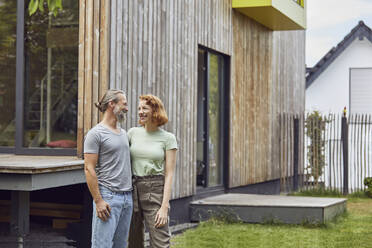 Romantic couple looking at each other while standing outside tiny house in yard - MCF01287