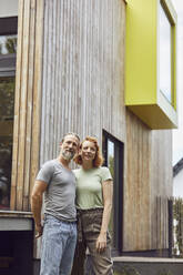 Thoughtful couple looking away while standing against tiny house in yard - MCF01289