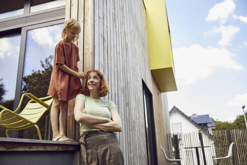 Girl tying mother's hair while standing outside tiny house - MCF01299