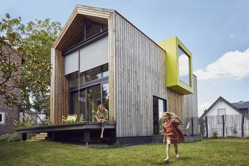 Mother looking at cheerful daughter running in yard while sitting outside tiny house - MCF01303