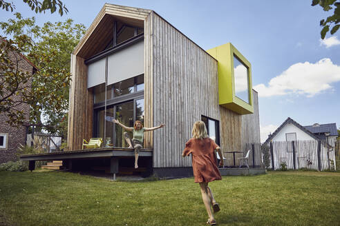 Girl running towards happy mother sitting outside tiny house - MCF01304