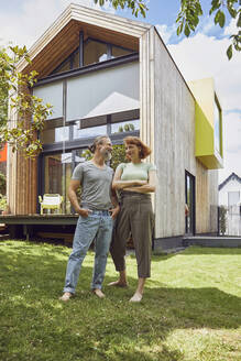 Mature man with hands in pockets looking at woman while standing outside tiny house - MCF01315