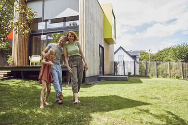 Cheerful parents with daughter standing against tiny house in yard - MCF01318