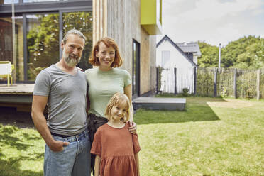 Smiling family standing outside tiny house in yard - MCF01320