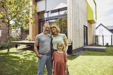 Smiling parents with daughter standing against tiny house in yard - MCF01321