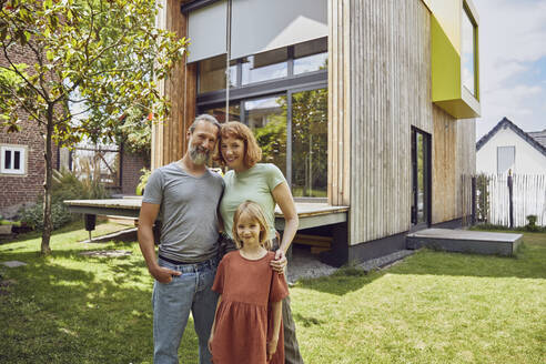 Smiling daughter standing with parents against tiny house in yard - MCF01322