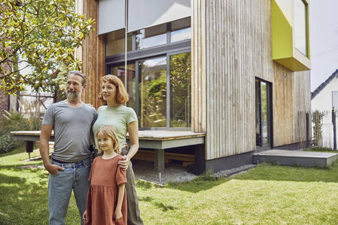 Lächelnde Familie schaut weg, während sie vor einem kleinen Haus im Hof posiert - MCF01323