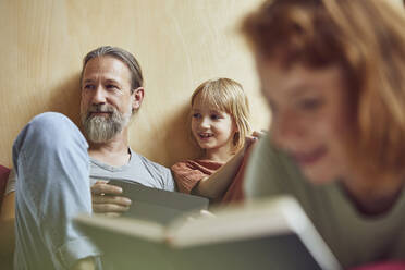 Woman reading book while father and daughter looking away in background at home - MCF01347
