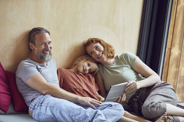 Smiling parents with daughter using digital tablet while lying on bed at home - MCF01350