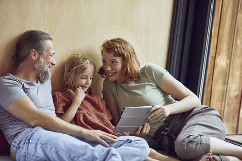 Smiling parents with daughter using digital tablet while relaxing on bed at home - MCF01351