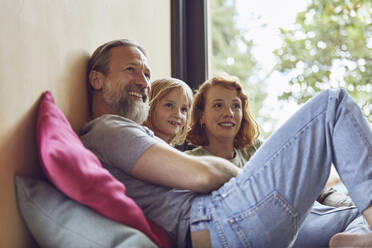 Parents and daughter looking away while relaxing on bed at home - MCF01352