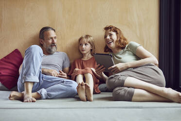 Cheerful woman holding digital tablet relaxing with family on bed at home - MCF01354