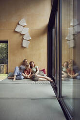 Family looking through window while relaxing on bed at home - MCF01355
