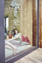 Family relaxing on bed at home seen through window - MCF01356