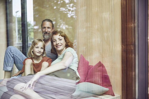 Smiling family relaxing on bed at home seen through window - MCF01357