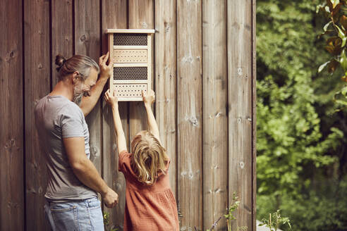 Vater und Tochter hängen Insektenhotel an die Wand - MCF01359