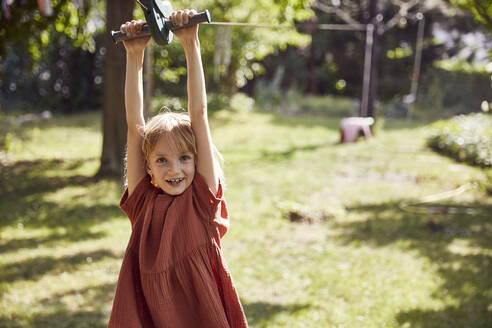 Fröhliches Mädchen, das sich an einem Spielgerät im Freien auf dem Hof aufhängt - MCF01379