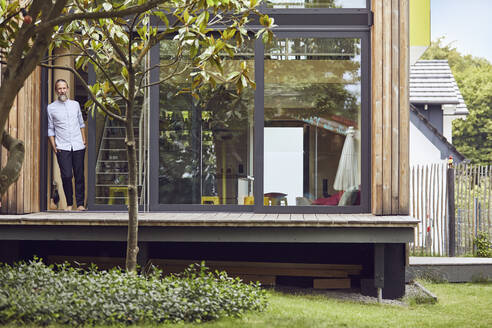 Thoughtful mature man standing at entrance of tiny house - MCF01392