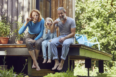 Parents with daughter brushing teeth while sitting outside tiny house - MCF01413