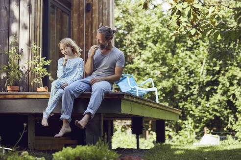 Father and daughter brushing teeth while sitting outside tiny house - MCF01416