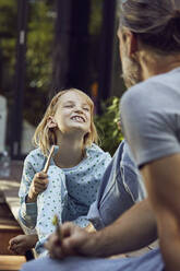 Mädchen zeigt dem Vater die Zähne, während sie mit ihm im Garten bürstet - MCF01418