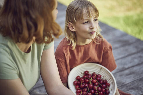 Nahaufnahme von Mutter und Tochter, die im Garten sitzend Kirschen essen - MCF01447