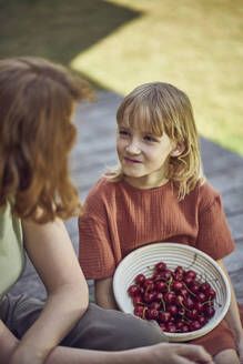 Mutter sitzend und Kirschen essend im Garten sitzend - MCF01448