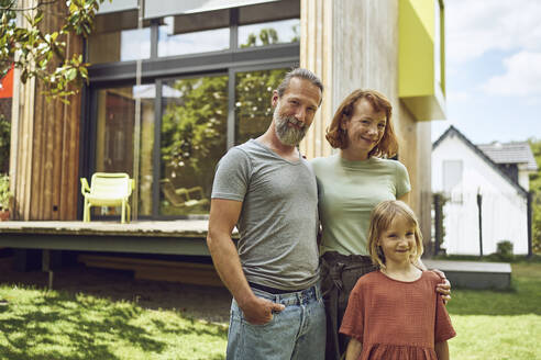 Smiling family posing while standing against tiny house in yard - MCF01450