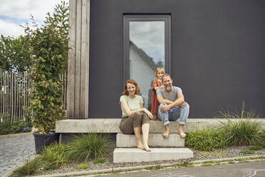 Smiling parents with girl sitting on steps outside tiny house - MCF01452