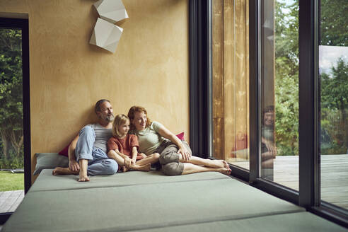 Parents with daughter looking through window while relaxing on bed at home - MCF01456